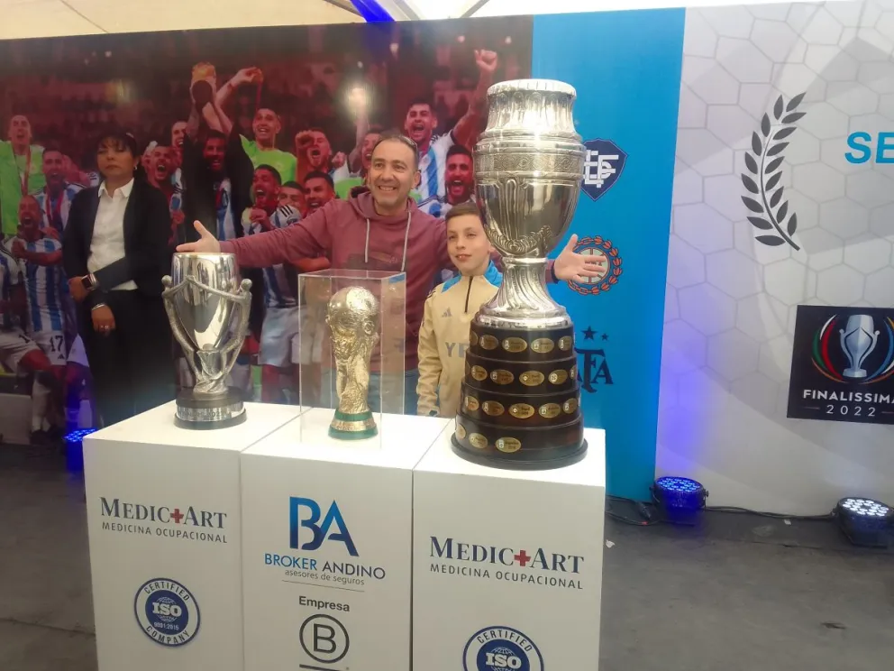 Felices. Papá e hijo se sacan una imagen con las tres Copas obtenidas por la Scaloneta.