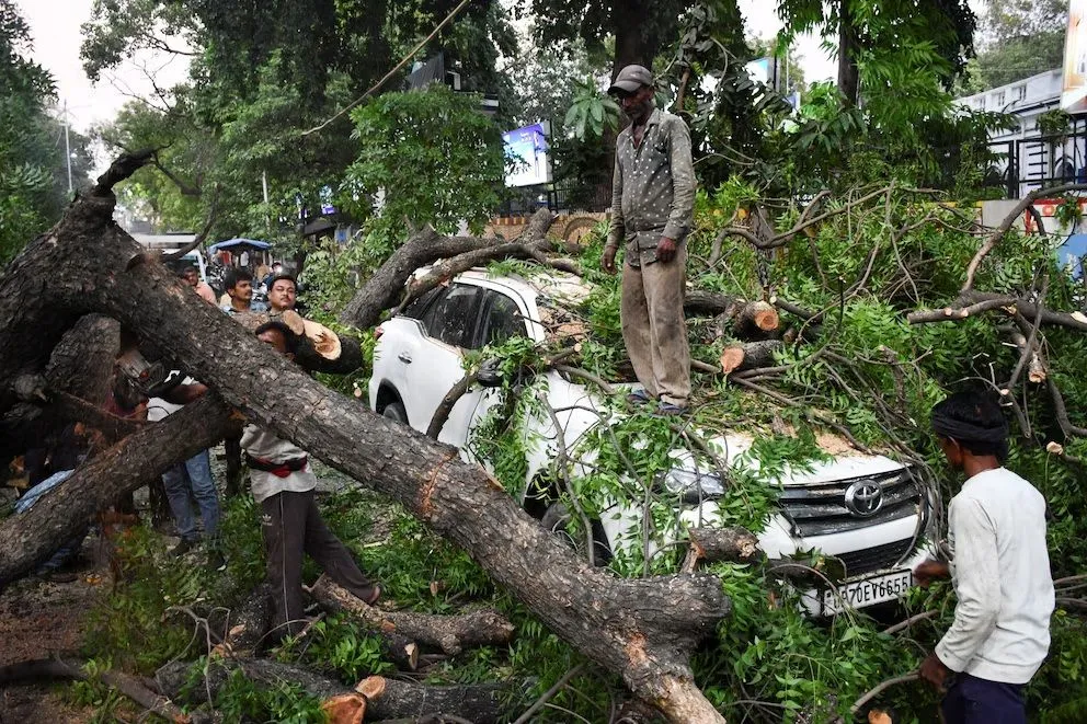 Varias personas retiran un árbol caído sobre un coche durante una fuerte tormenta en Prayagraj, en el estado norteño de Uttar Pradesh, India.