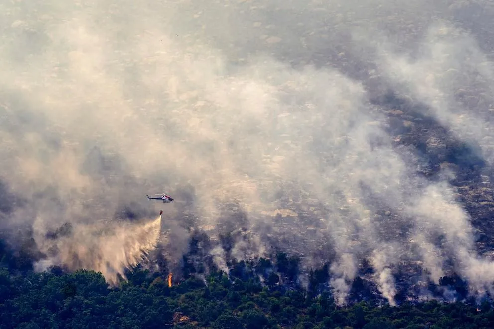 Un helicóptero de extinción descarga agua sobre un foco de incendio y una extensa zona de vegetación cubierta por humo en la provincia de Ávila.